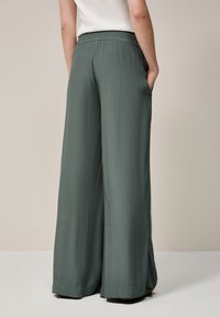 Wide-legged pants in muted green fabric, featuring a comfortable elastic waistband and side pockets, with a soft texture and flowing design.