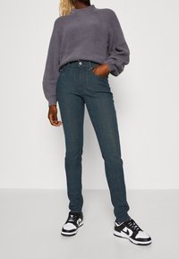 Lehký, žebrovaný šedý pletený svetr s oversized rukávy v kombinaci s tmavě modrými slim-fit džíny a černobílými sportovními teniskami.