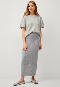 Lichtgrijze gebreide trui met korte mouwen, gecombineerd met een bijpassende lange kokerrok. Zilveren platte schoenen maken de outfit af. Eenvoudig en monochroom ontwerp.