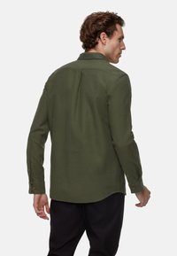 Olijf groene langemouwen shirt van zachte stof, met een klassieke kraag, knoopmanchetten en een gebogen onderkant. Zichtbaar rugpand detail.