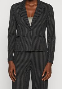 Czarny żakiet w prążki z wysmuklonym kołnierzem, zapięcie na jeden guzik, dwie przednie kieszenie, dopasowany krój i fakturowany materiał.