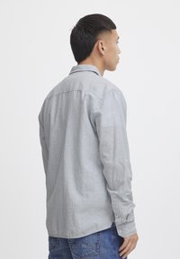 Camicia a maniche lunghe di colore grigio chiaro con sottili righe verticali, dotata di colletto con bottoni e bottoni ai polsini, realizzata in un tessuto testurizzato.