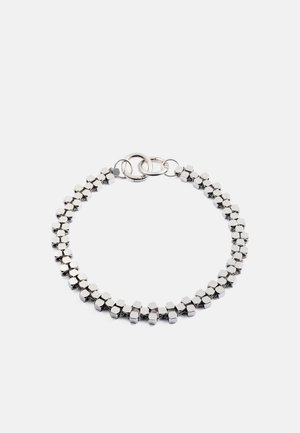 Hopeaketju, jossa on toisiinsa kytkettyjä kuusikulmaisia metallilinkkejä, sileä pinta ja turvallinen solkilukko. Yksinkertainen, geometrinen muotoilu.