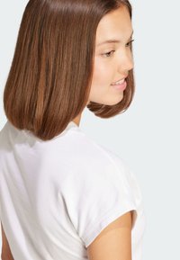 White cotton t-shirt with short sleeves, slightly rolled cuffs, featuring a round neckline and smooth texture. Background is light gray.