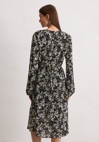 Schwarzes Blumenkleid mit weißen und grünen Mustern, langen Ärmeln und Taillenknoten. Weicher Stoff, knielanges Design und runder Halsausschnitt.