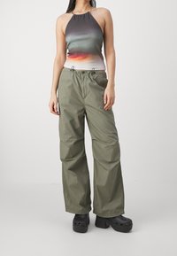 Top na halter z gradientowymi kolorami; luźne oliwkowe spodnie; czarne klapki z wycięciami; prosty design z elastycznym pasem.