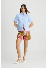 Camicia a maniche corte a righe blu chiaro, pantaloni corti a fantasia nei toni del rosa e del marrone, e décolleté bianche con cinturino alla caviglia. La camicia corta presenta una chiusura frontale con bottoni.