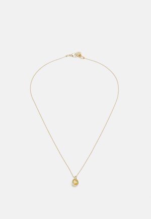 Collier délicat en chaîne d’or avec un petit pendentif en pierre précieuse jaune ovale, présenté sur un fond gris clair uni.
