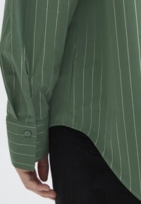 Grünes, gestreiftes Langarmhemd mit spitzem Kragen, geknöpften Manschetten und abgerundetem Saum. Der Stoff wirkt glatt und leicht.