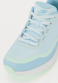 Light blue athletic shoe with mesh upper, tonal lace design, and a green accent sole. Notable for its lightweight construction and texture.