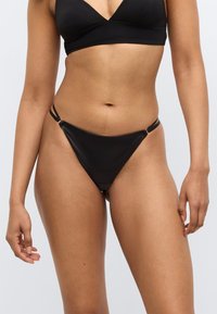 Μαύρο κάτω μέρος μπικίνι με κομψό σχεδιασμό, λεπτές πλευρικές ράντες και ελάχιστη κάλυψη. Κατασκευασμένο από λείο υλικό, παρουσιάζοντας ένα απλό, σύγχρονο στυλ.