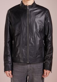 Schwarze Lederjacke mit hohem Kragen, Frontreißverschluss und zwei seitlichen Taschen. Besitzt eine glatte Textur und Paneel-Details auf der Vorderseite.