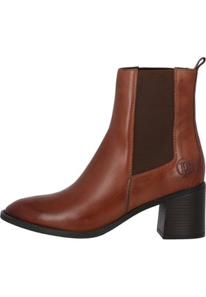 Brun læderankelstøvle med elastisk sidepanel, blokhæl og en træktab bagpå, der viser en lille præget logo nær hælen.