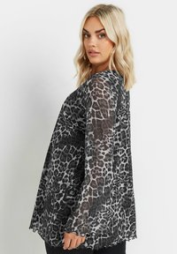 Transparent svart och grå leopardmönstrad topp med långa ärmar, rundad nederkant och vågig kant. Lättviktsmaterial med en lös passform.