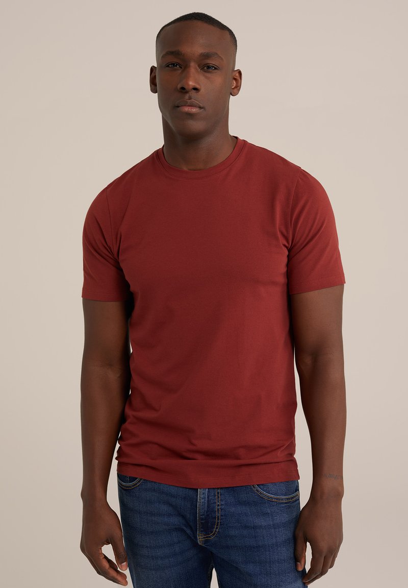 Rde majica iz bombaža s kratkimi rokavi in okroglo ovratnikom, v kombinaciji z modrimi jeans hlačami. Tkanina se zdi gladka in lahka.