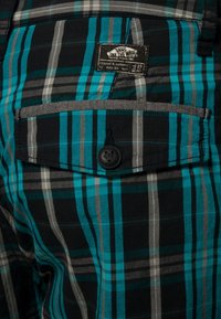 Pantaloni a quadri strutturati con strisce nere, turchesi e grigie. Presentano una tasca posteriore con bottone e un'etichetta del marchio tessuta.