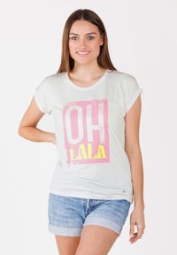 Hellgraues Baumwoll-T-Shirt mit umgeschlagenen Ärmeln, das einen pinken und gelben Grafikdruck mit dem Text "OH LALA" zeigt. Kombiniert mit Jeansshorts.