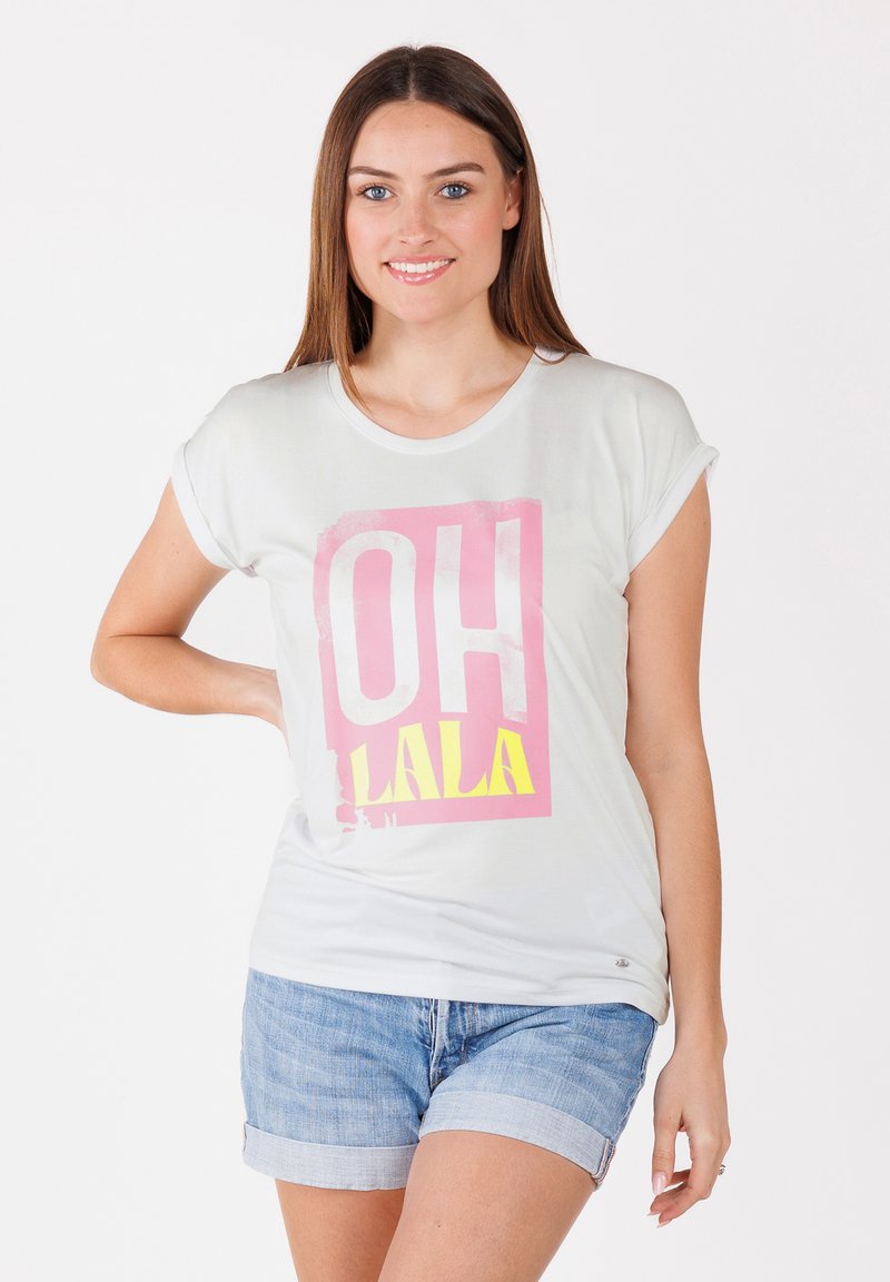Hellgraues Baumwoll-T-Shirt mit umgeschlagenen Ärmeln, das einen pinken und gelben Grafikdruck mit dem Text "OH LALA" zeigt. Kombiniert mit Jeansshorts.