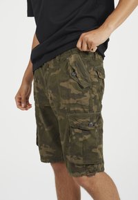 Καμουφλάζ cargo σορτς σε πράσινους τόνους, κατασκευασμένα από ανθεκτικό ύφασμα, με πολλαπλές τσέπες, κουμπιά διακοσμητικά και άνετη εφαρμογή.