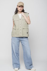Khaki vest featuring a zip front, multiple large pockets, and a relaxed fit, paired with light blue wide-leg jeans and a beige cap.