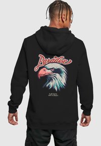 Felpa nera con cappuccio caratterizzata da una grafica colorata di un'aquila sul retro, con la scritta "Paradise" e la frase "tutto inizia con un sogno" sotto.