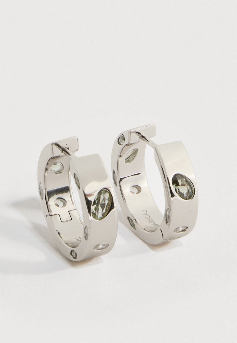 Hõbedast rõngakujulised kõrvarõngad, mille ümber rõngas on ühtlaselt paigutatud mitu väikest läbipaistvat vääriskivi, valgel taustal.