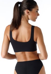 Reggiseno sportivo nero con design senza cuciture, spalline larghe e vestibilità aderente. Texture liscia e stile minimalista. Indossato con pantaloni alti coordinati.