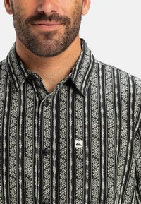 Camisa de botones a rayas blancas y negras con un patrón floral, que presenta una etiqueta de marca y un cuello. Tejido texturizado con un ajuste relajado.