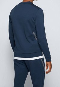 Felpa blu navy con scollo rotondo, polsini e orlo a costine. Presenta un pannello laterale testurizzato con motivo geometrico. Tessuto dalla texture morbida.