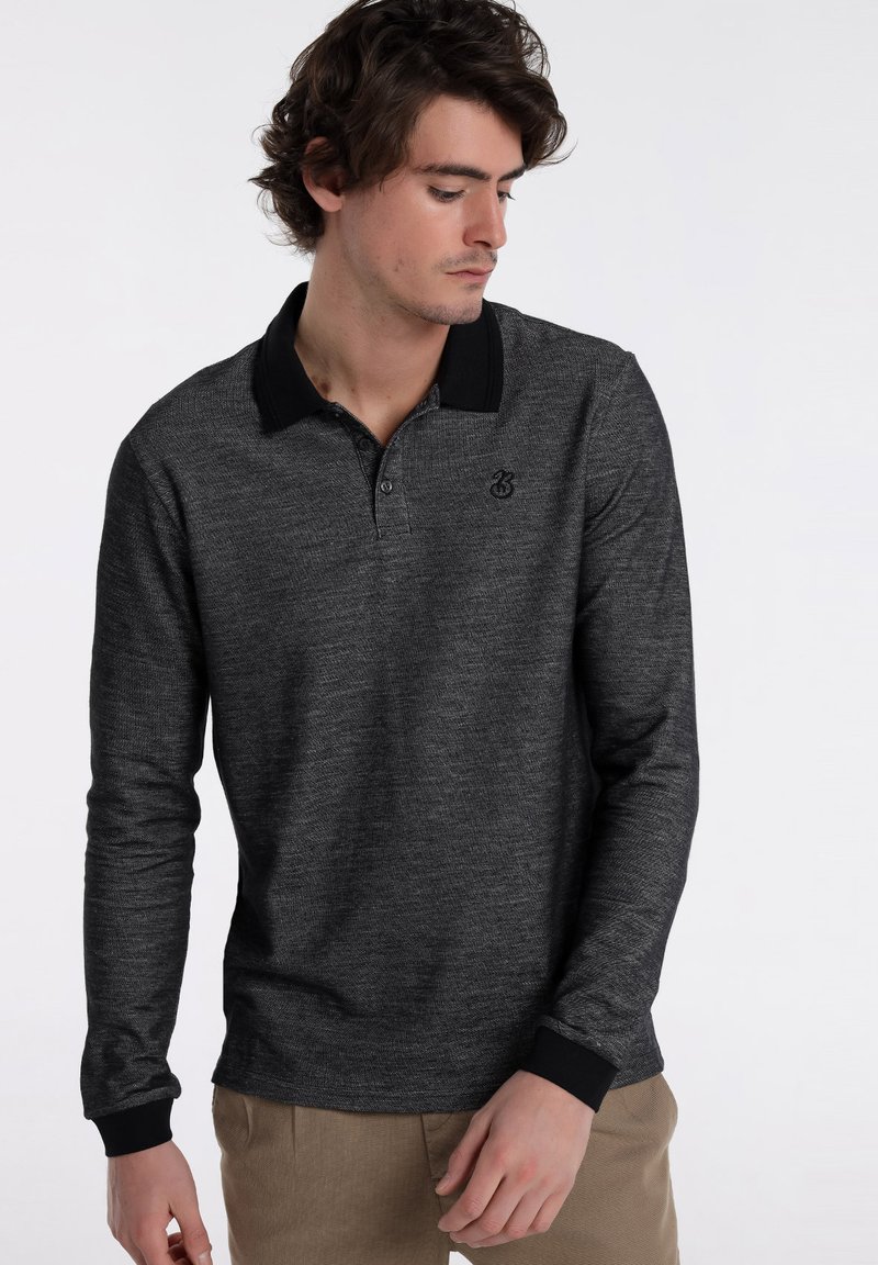 Graues Langarm-Polo-Shirt mit schwarzem Kragen und Manschetten, das ein dezentes Muster aufweist und ein kleines Logo auf der linken Brustseite trägt.