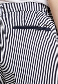 Tessuto a righe blu navy e bianco, con una tasca con zip sul retro. La texture appare liscia con dettagli di cucitura precisi.