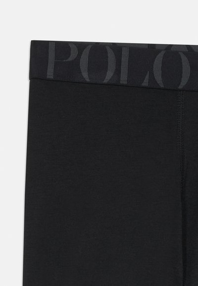Juodos leggingai su plačiu juosmens diržu, turinčiu reljefinį 'POLO' logotipą. Medžiaga atrodo glotni, su minimaliu tekstūros visame paviršiuje.