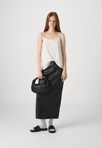 Hvit strikket tanktop, svart lær maxiskjørt, svart håndveske, hvite sokker, svarte sandaler. Glatte teksturer, lagdelt design.