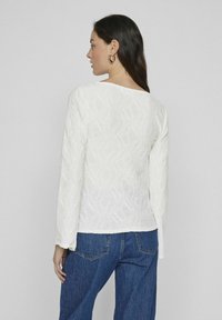 Maglietta bianca a maniche lunghe con un motivo a onde testurizzato, scollatura rotonda e un design aderente, abbinata a pantaloni in denim blu.