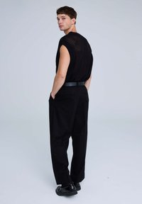 Top nero a maniche corte, lavorato a maglia con tessuto a trama aperta e texture a coste, abbinato a pantaloni neri dal taglio morbido e scarpe nere lucide.