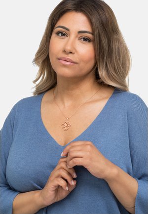 Kupferbaum-Anhänger-Halskette an einer roségoldenen Kette, getragen über einem blauen V-Ausschnitt-Oberteil, mit glatter Textur und minimalistischem Design.