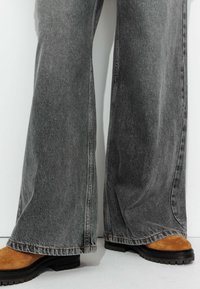 Pantalons en denim gris évasés avec une texture douce et des détails de couture visibles, associés à des bottines en suedine marron avec des semelles épaisses.