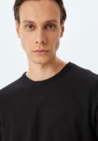 Sort langærmet skjorte med et tekstureret vaffelmønster, rund hals og almindelig pasform. Glat stof med minimal dekoration.