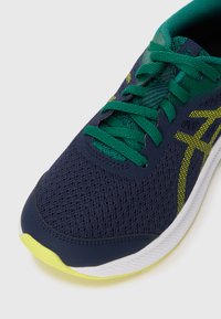 Baskets de course bleu foncé avec des lacets et des accents verts, tige en maille et détails jaunes près de la semelle, présentant une surface texturée.