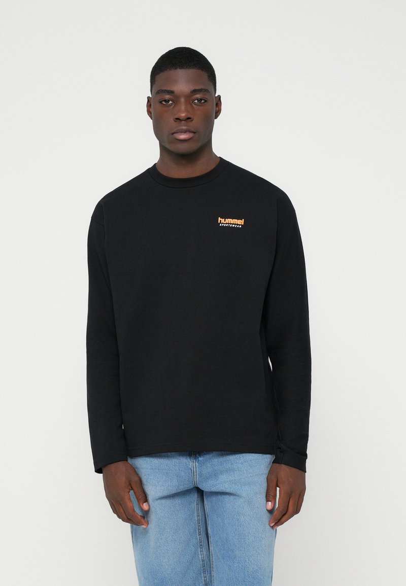 Camisa negra de manga larga con cuello redondo, que presenta un logo "hummel" naranja en el pecho. La tela parece suave y ligeramente elástica.