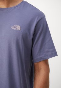 Kortermet t-skjorte med rund hals i støvete lilla stoff, med en liten brodert logo på venstre brystområde. Glatt tekstur.