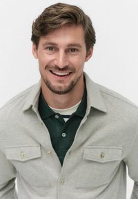 Herren Hemd in Hellgrau mit gewebtem Design und zwei Vorderaschen, über einem dunkelgrünen Poloshirt mit gestreiftem Kragen getragen. Angenehme Textur, lässige Passform.