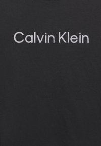 Černé bavlněné tričko s bílým logem "Calvin Klein" a pruhovanou texturou. Kulatý výstřih. Jednoduchý, minimalistický design.