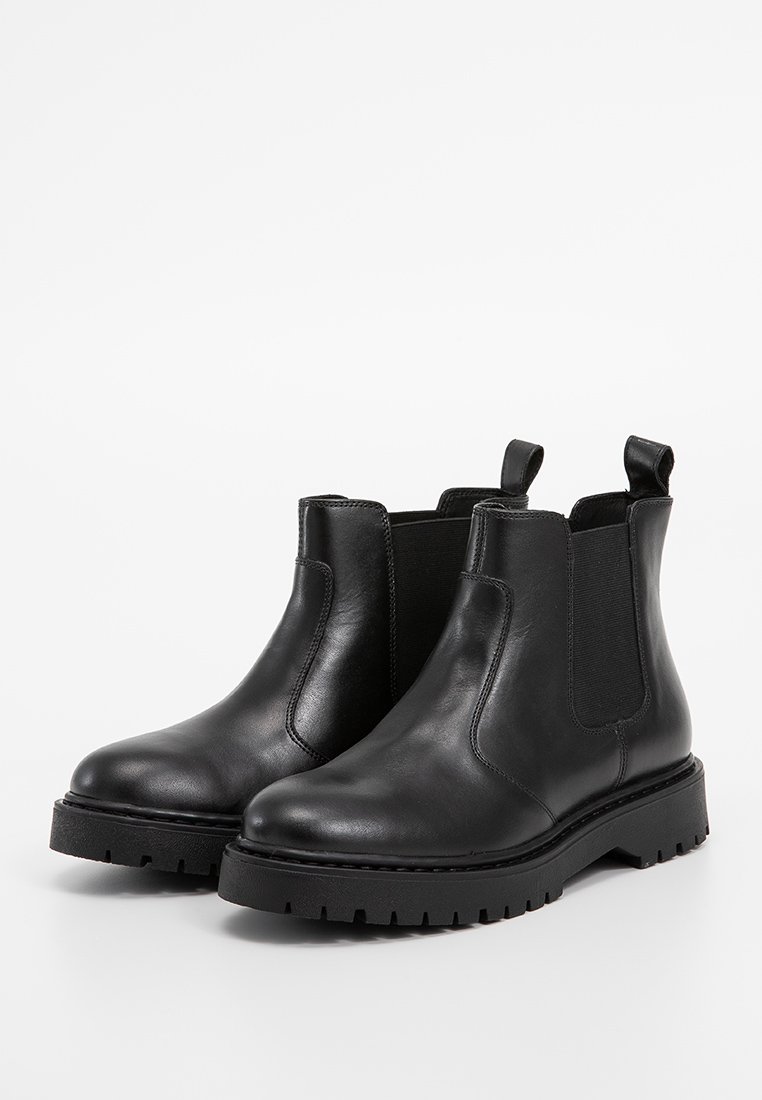Bottines Chelsea en cuir noir avec des panneaux élastiques sur les côtés, un bout arrondi et une semelle noire épaisse avec un motif de traction texturé.