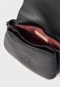 Borsa in pelle nera testurizzata con patta aperta, che mostra l'interno in tessuto color amaranto e un'etichetta beige all'interno.