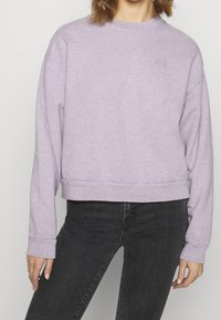 Light purple sweatshirt with a crew neck, long sleeves, and cropped hem. Features ribbed cuffs and a subtle logo embroidered on the chest.