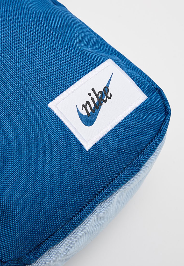 Cojín de tela azul con superficie texturizada, con una etiqueta blanca que lleva el logo de "Nike" y un swoosh azul, diseño con esquinas redondeadas.