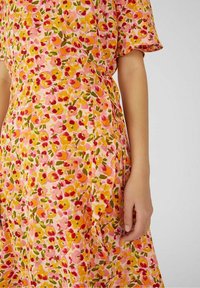 Kukkakuvioinen kietaisumekko vaaleanpunaisesta kankaasta, jossa on keltaisia, punaisia ja vihreitä kukkamalleja. Lyhyet hihat ja vyötäröllä solmittava yksityiskohta.