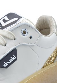 Sneaker bianca in pelle con accenti dorati in glitter, fodera testurizzata beige chiaro, lacci piatti e un patch con logo sulla linguetta.