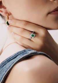 Sydänmuotoinen smaragdiriipus, jossa on timanttien pavé, asetettu hopeaan. Kullankeltainen rengaskorvakoru, jossa on yhteensopiva smaragdi, käytetty denimpinnoitteen kanssa.